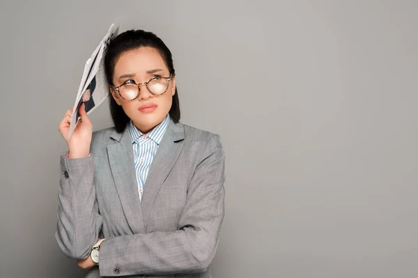 Sad young businesswoman in eyeglasses holding newspaper on grey background — Stock Photo