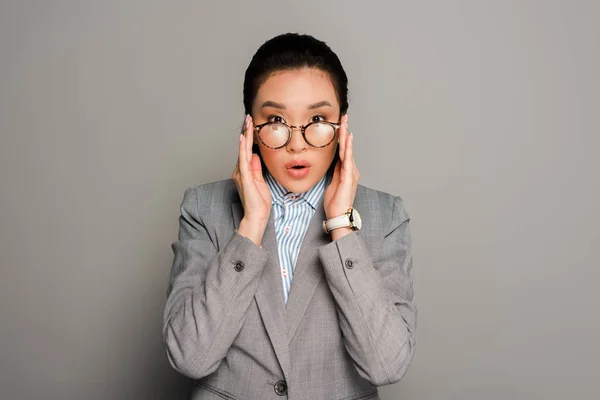 Sorprendido joven mujer de negocios en gafas sobre fondo gris - foto de stock