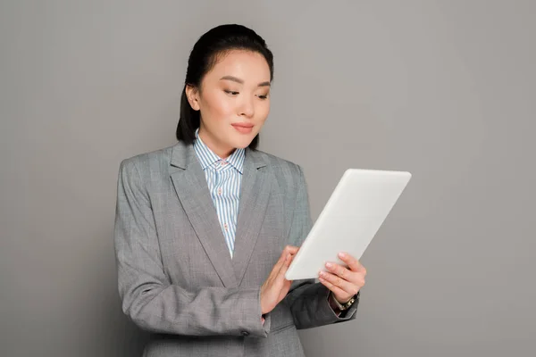 Junge Geschäftsfrau im Anzug mit digitalem Tablet auf grauem Hintergrund — Stockfoto