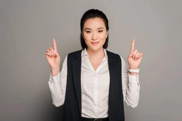 Улыбающаяся молодая деловая женщина, указывающая пальцами на сером фоне — стоковое фото