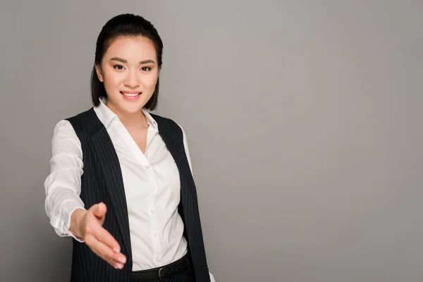 Усміхнена молода бізнес-леді дає руку на сірому фоні — стокове фото