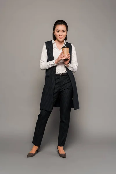 Smiling young businesswoman holding coffee to go on grey background — Stock Photo