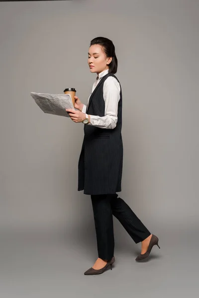 Молода бізнес-леді читає газету і п'є каву на сірому фоні — стокове фото