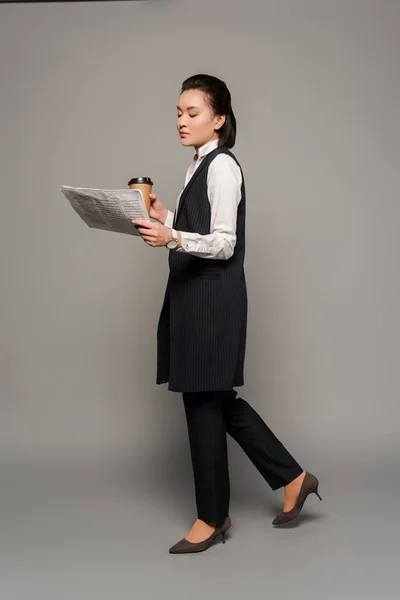 Young businesswoman reading newspaper and drinking coffee on grey background — Stock Photo