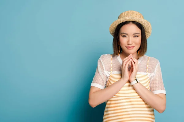 Astuta chica asiática en rayas vestido amarillo y sombrero de paja sobre fondo azul - foto de stock