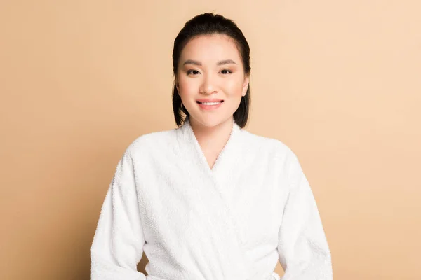 Sonriente hermosa asiática mujer en albornoz en beige fondo - foto de stock