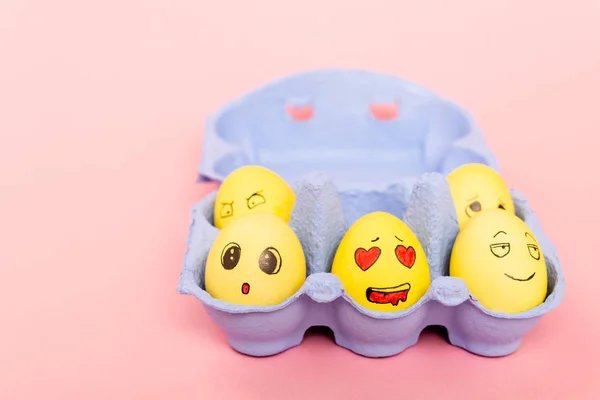 Selective focus of painted Easter eggs with facial expressions in egg tray on pink — Stock Photo