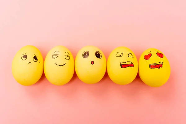 Vista superior de huevos de Pascua pintados con diferentes expresiones faciales sobre fondo rosa - foto de stock