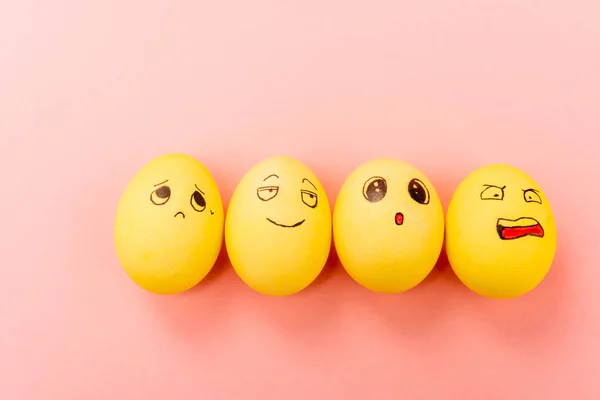 Верхний вид пасхальных яиц с различными смешными выражениями лица на розовом фоне — стоковое фото