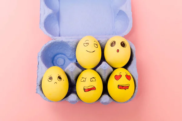 Top view of colorful easter eggs with facial expressions in egg tray on pink background — Stock Photo