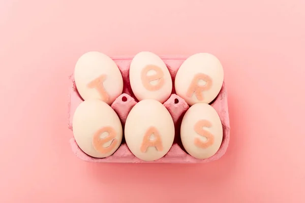 Vue en angle élevé des œufs de poulet avec lettrage de Pâques dans le bac à œufs sur rose — Photo de stock