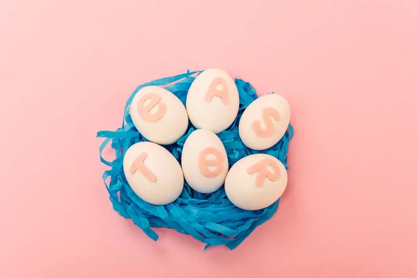 Vue en angle élevé des œufs de poulet avec lettrage de Pâques dans le nid sur fond rose — Photo de stock