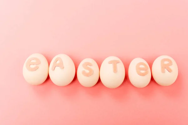 Top view of chicken eggs with easter lettering on pink background — Stock Photo