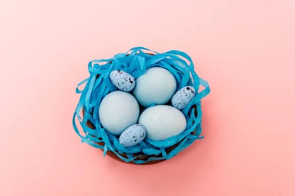 Vue en angle élevé des oeufs de caille et de poulet dans le nid bleu sur fond rose, concept de Pâques — Photo de stock