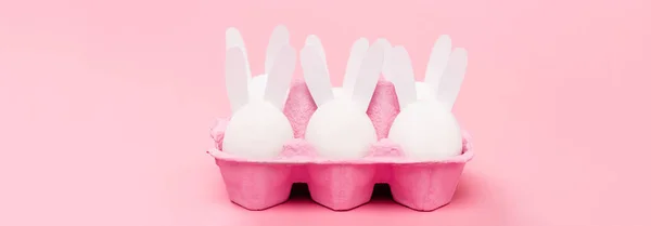 Conejitos decorativos de Pascua en bandeja de huevo sobre fondo rosa, plano panorámico - foto de stock