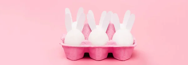 Conejitos decorativos de Pascua en bandeja de huevo sobre fondo rosa, plano panorámico - foto de stock