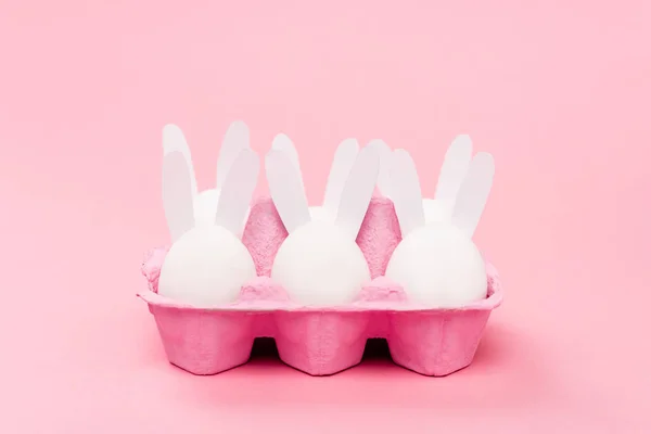 Lapins de Pâques décoratifs dans un bac à œufs sur fond rose — Photo de stock