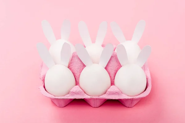 Conejitos decorativos de Pascua en bandeja de huevo en rosa - foto de stock