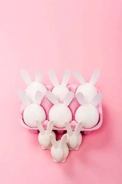 Vista de ángulo alto de conejos de Pascua decorativos con bandeja de huevo sobre fondo rosa - foto de stock