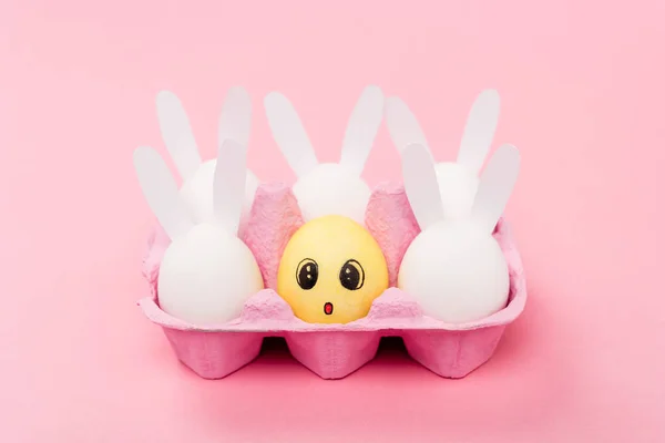 Lapins décoratifs et œuf jaune avec expression faciale surprise sur rose, concept de Pâques — Photo de stock