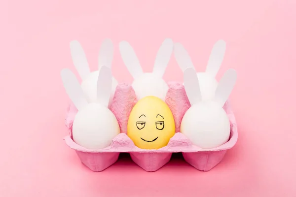 Conigli decorativi e uovo giallo con espressione facciale sorridente su rosa, concetto pasquale — Foto stock