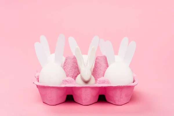 Coelhos de Páscoa na bandeja de ovos no fundo rosa — Fotografia de Stock