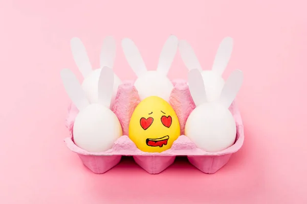 Lapins décoratifs et oeuf jaune avec expression faciale émue sur rose, concept de Pâques — Photo de stock