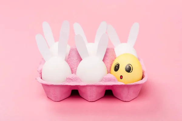 Coelhos decorativos e ovo amarelo com expressão facial chocada em rosa, conceito de Páscoa — Fotografia de Stock