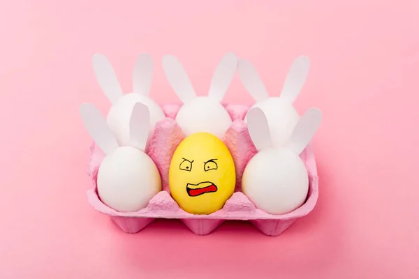 Coelhos decorativos e ovo amarelo com expressão facial irritada em rosa, conceito de Páscoa — Fotografia de Stock