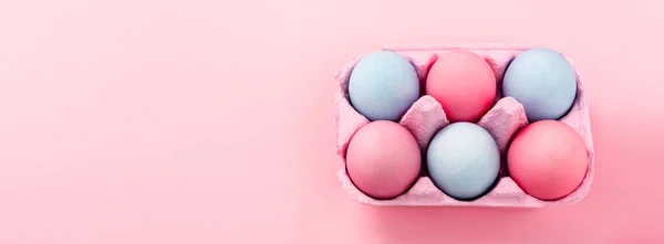 Vista de ángulo alto de huevos de Pascua coloridos en bandeja de huevo sobre fondo rosa, tiro panorámico - foto de stock