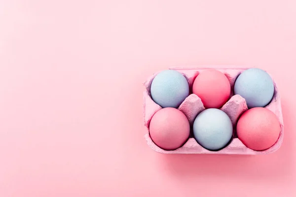 Visão de alto ângulo de ovos de páscoa pintados em bandeja de ovo em rosa — Fotografia de Stock