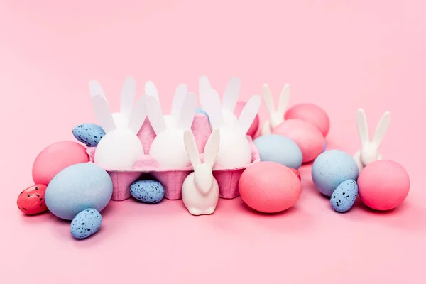 Egg tray with colorful easter eggs and decorative bunnies on pink background — Stock Photo