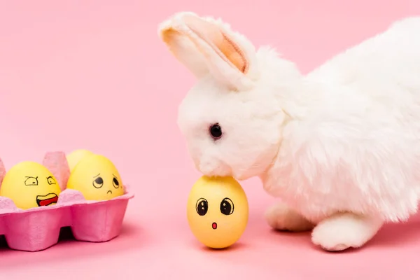 Conejito de Pascua y coloridos huevos de pollo con expresiones faciales sobre fondo rosa - foto de stock