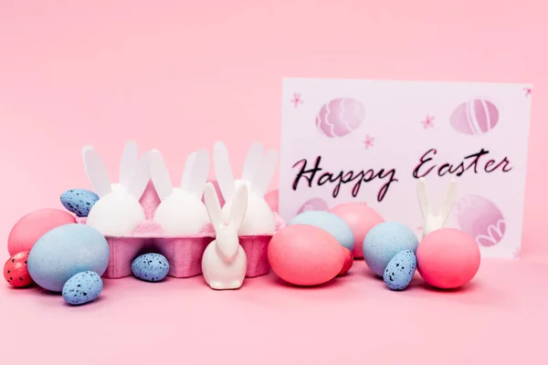 Colorful eggs, decorative bunnies and card with happy easter lettering on pink — Stock Photo