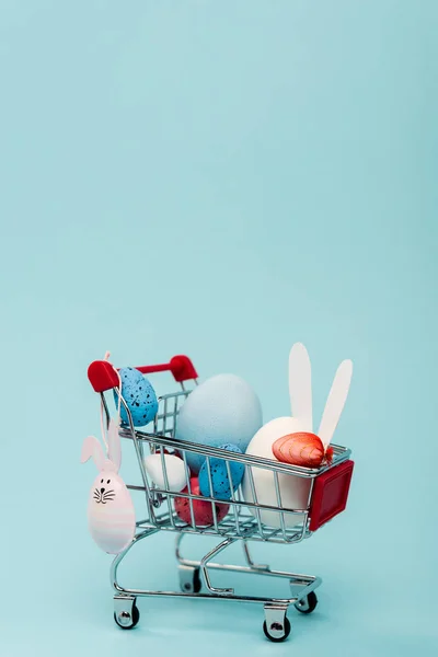 Huevos coloridos de Pascua y conejos decorativos en el carrito en azul - foto de stock