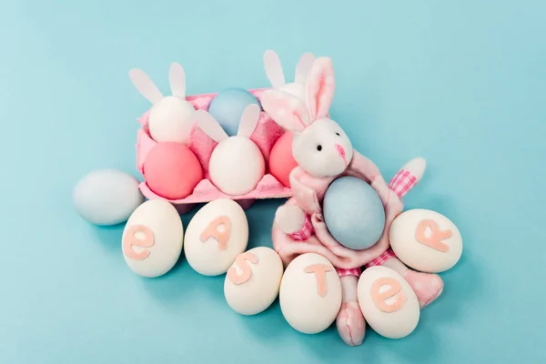 Œufs de poulet peints avec lettrage de Pâques et lapins décoratifs sur fond bleu — Photo de stock