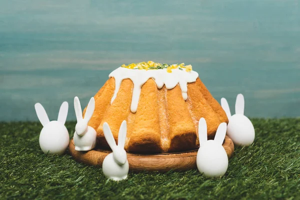 Easter cake on wooden board and decorative bunnies on grass — Stock Photo
