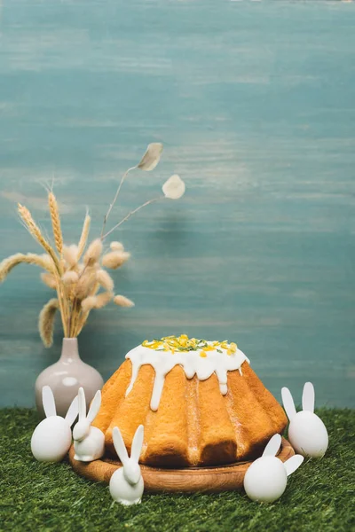 Pan de Pascua con conejos decorativos y jarrón con sauce y trigo sobre hierba - foto de stock