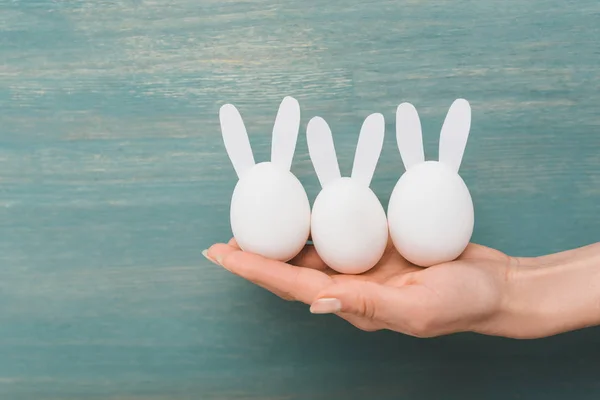 Cropped view of female hand with decorative easter bunnies on wooden background — Stock Photo