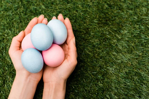 Vista recortada de la mujer sosteniendo coloridos huevos de Pascua sobre fondo verde - foto de stock