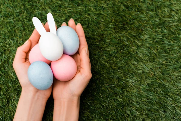 Vista recortada de la mujer sosteniendo coloridos huevos de pollo y conejito de Pascua sobre fondo verde - foto de stock