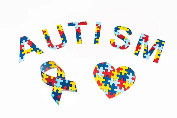 Vista de alto ângulo de letras de quebra-cabeça de autismo, coração decorativo e fita de consciência isolada em branco — Fotografia de Stock