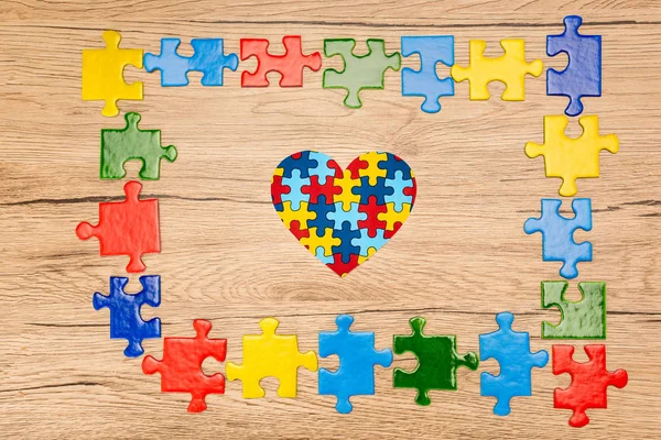 Vista superior do coração decorativo com peças de quebra-cabeça em fundo de madeira, conceito de autismo — Fotografia de Stock
