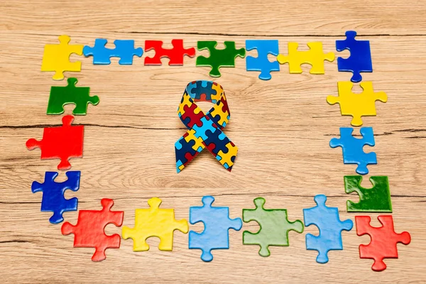 Ruban de sensibilisation avec des pièces colorées de puzzle sur fond en bois, concept d'autisme — Photo de stock