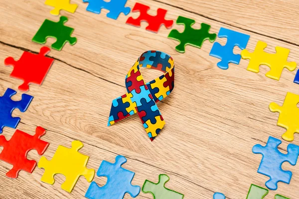 Vista de alto ângulo da fita de consciência com peças de quebra-cabeça em fundo de madeira, conceito de autismo — Fotografia de Stock