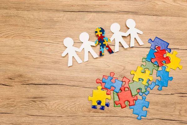 Високий кут зору спеціальної дитини з аутизмом серед інших і шматочків головоломки на дерев'яному фоні — стокове фото