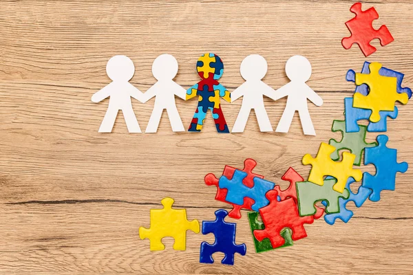 Top view of special kid with autism among another and pieces of bright colorful puzzle on wooden background — Stock Photo