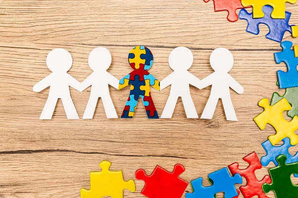 Top view of special kid with autism among another and pieces of multicolored puzzle on wooden background — Stock Photo