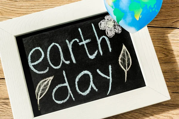 Top view of black board with earth day lettering and globe on wooden background — Stock Photo