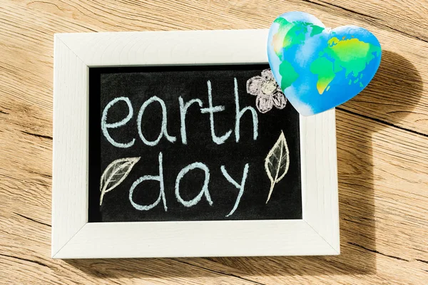 Draufsicht auf Tafel mit Earth Day Schriftzug und Globus auf Holzgrund — Stockfoto